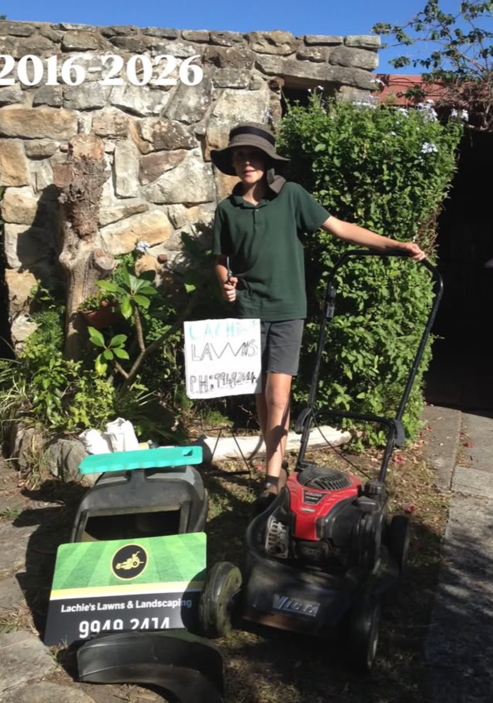 Lachie aged ten in 2016, standing with his mower and a hand-painted 'Lachie Lawns' sign